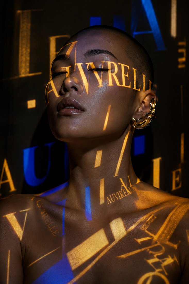 Gold and blue Auvirelle typography projected across a model's face
